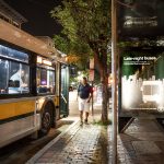 A customer boards a bus at night in front of a shelter advertising Late Night Buses